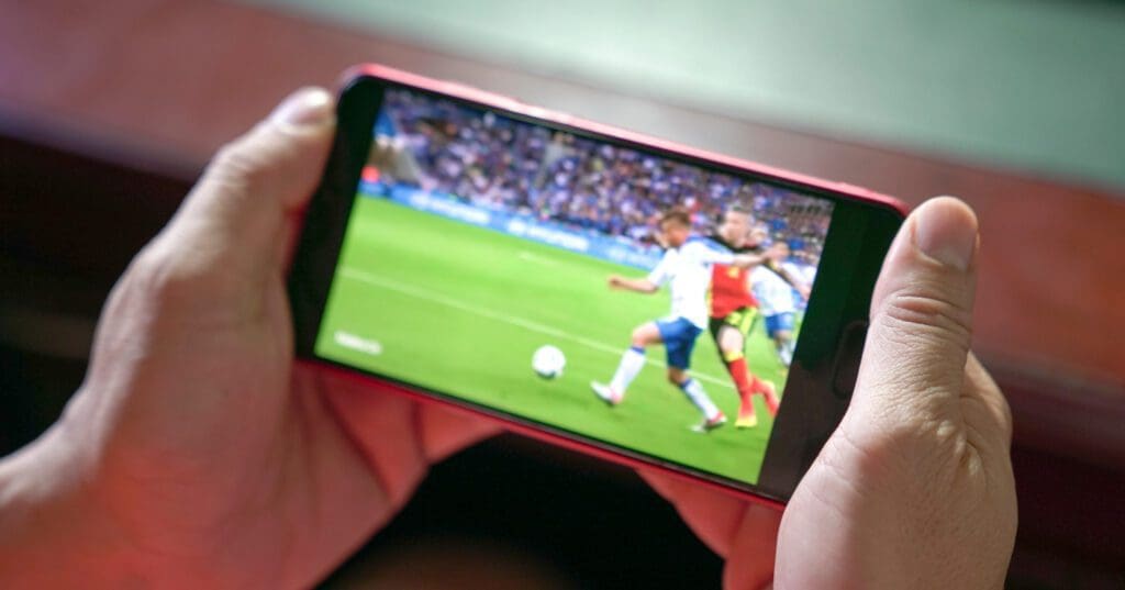 Hands holding a smart phone that is playing a clip from a football match